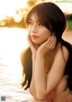 A woman with long black hair posing by the water.