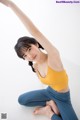 A woman in a yellow top and blue leggings doing a yoga pose.