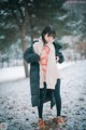 A woman standing in the snow wearing a jacket and scarf.