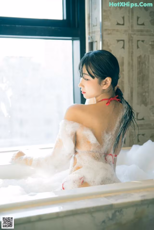 A woman in a bathtub with foam on her back.
