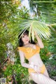 A woman in a yellow bikini posing in front of a palm tree.