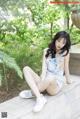 A woman sitting on a stone wall in a denim dress.