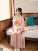 A woman in a pink kimono sitting on a bed.